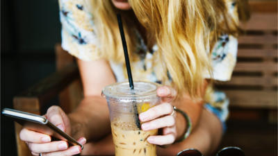 woman holding iced coffee and checking phone